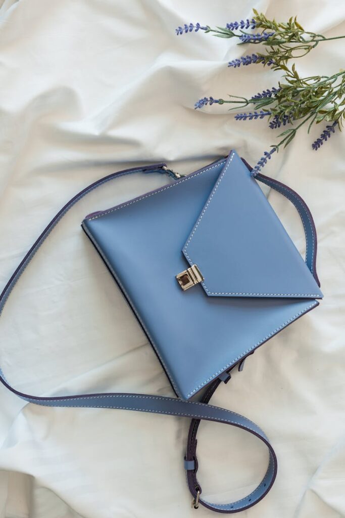 Stylish blue leather purse against a white background with lavender accents, perfect for chic fashion.